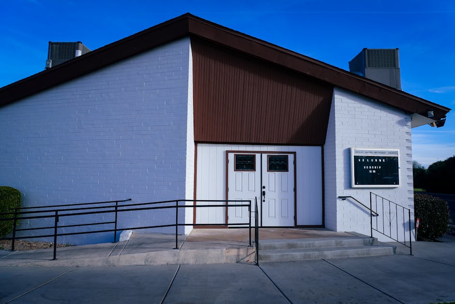 Workers installing metal roofing panels on a low community building surrounded by redwood trees